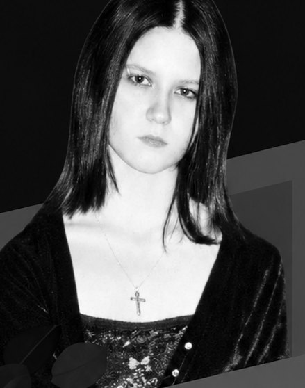 Sophie Lancaster, photographed with long dark hair, a velvet jacket and a cross necklace, looking directly at the camera